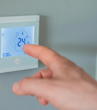 Main ajustant la température sur un thermostat mural à écran tactile affichant une interface de régulation domestique